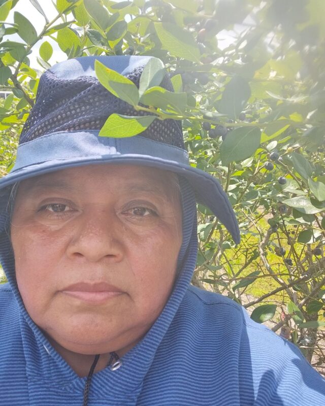 The image shows a close-up of a person outdoors, surrounded by dense green foliage.