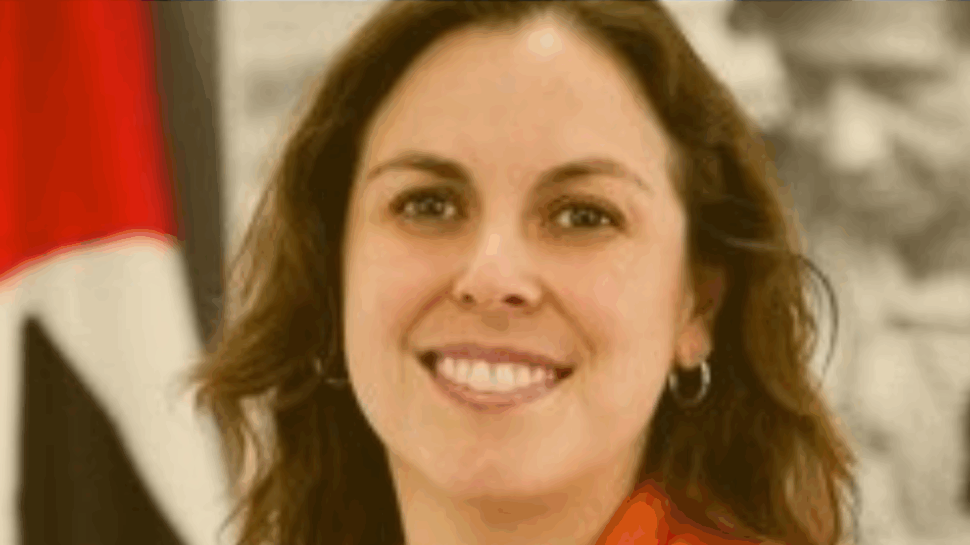 A woman wearing an orange shirt smiles warmly at the camera.