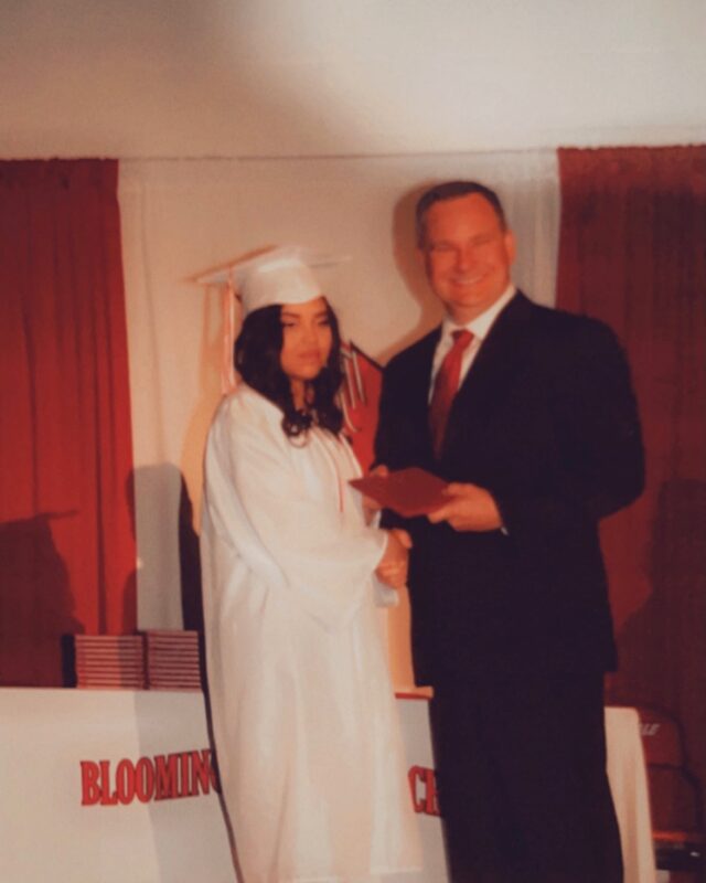 A man in a suit is shaking hands with a woman in a white graduation gown.