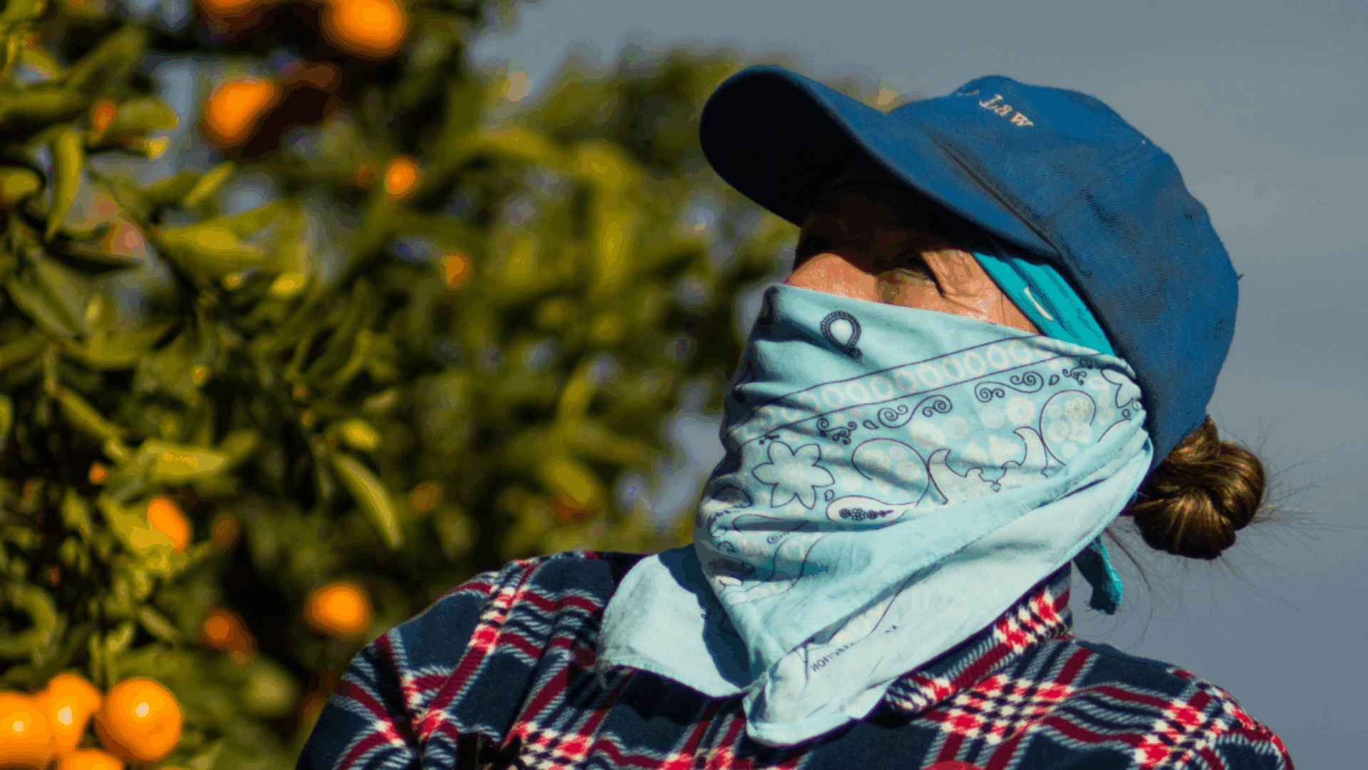 Una mujer con un pañuelo azul en la cabeza y una camisa a cuadros posa, reflejando un estilo relajado y moderno.
