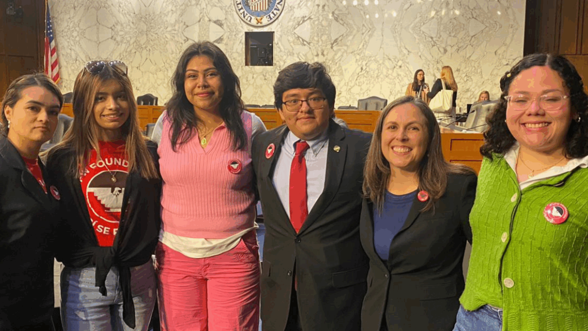 A group of activists stands together, facing congress in a hearing setting.