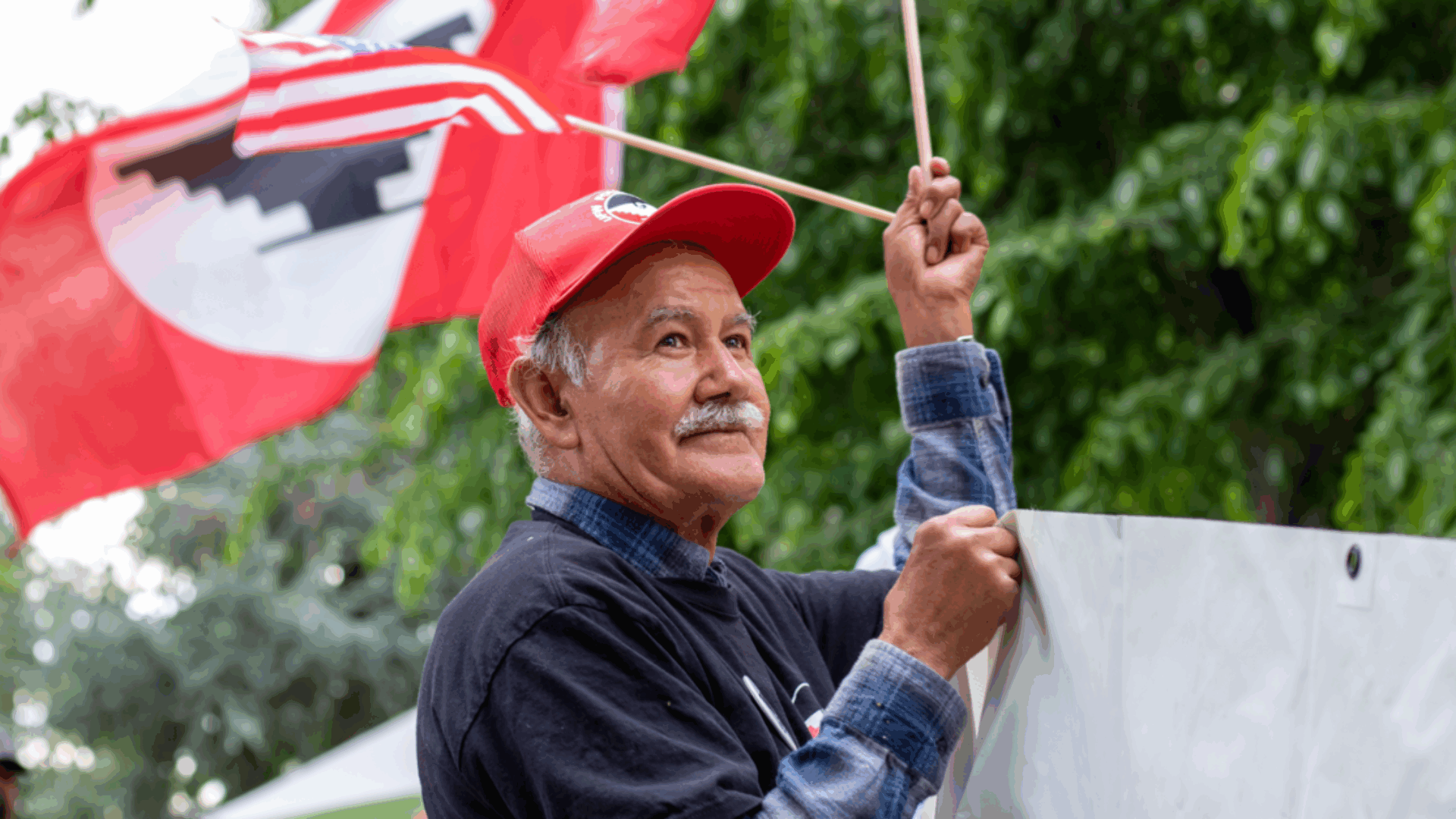 A man stands holding a flag in one hand and a sign in the other, expressing his message passionately.