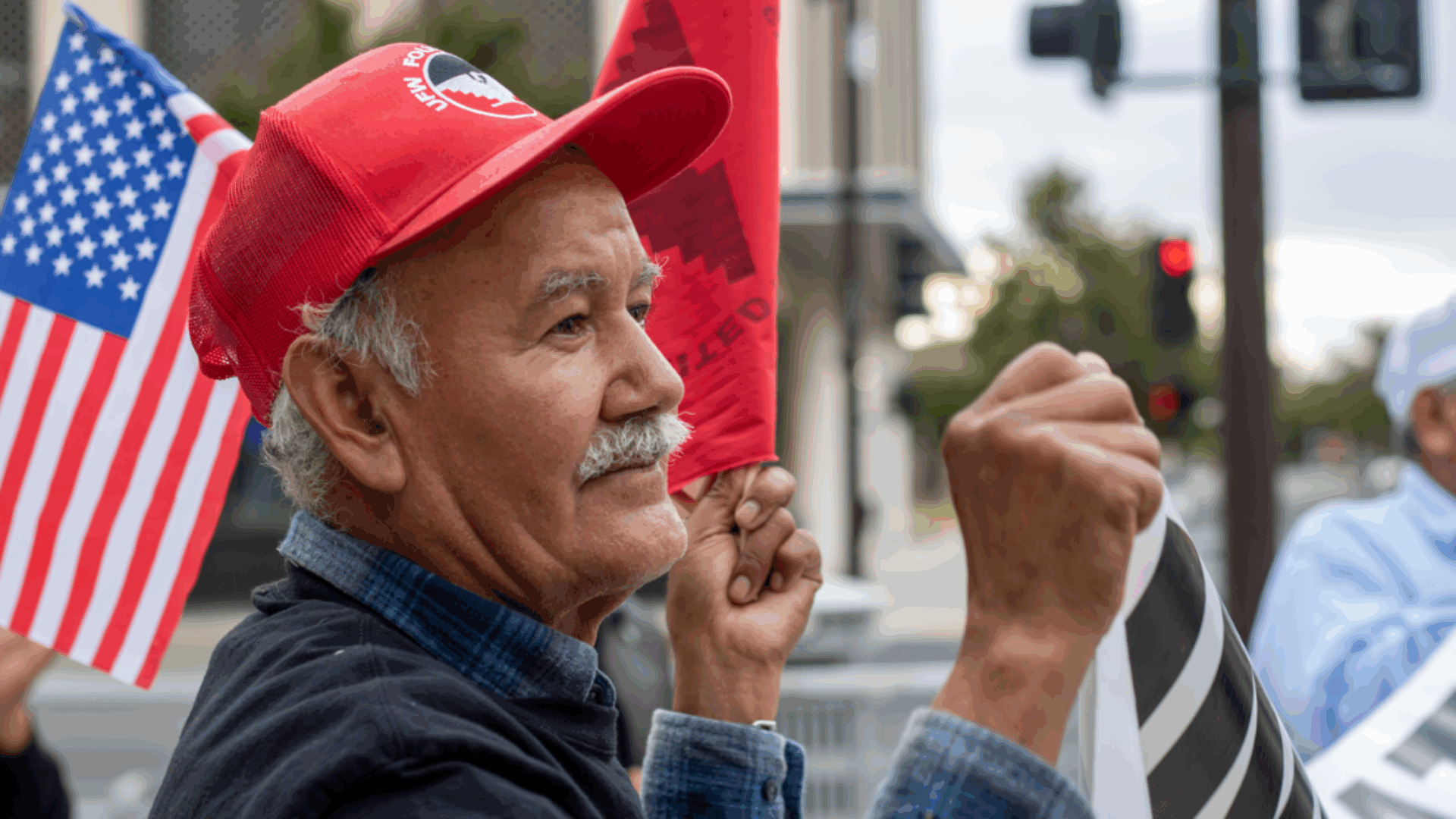 A man with a flag in one hand and a sign in the other, actively participating in a demonstration.