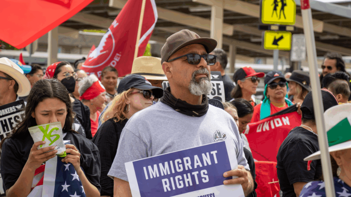 Un hombre sostiene un cartel que dice "Derechos de los inmigrantes," abogando por los derechos de los inmigrantes.
