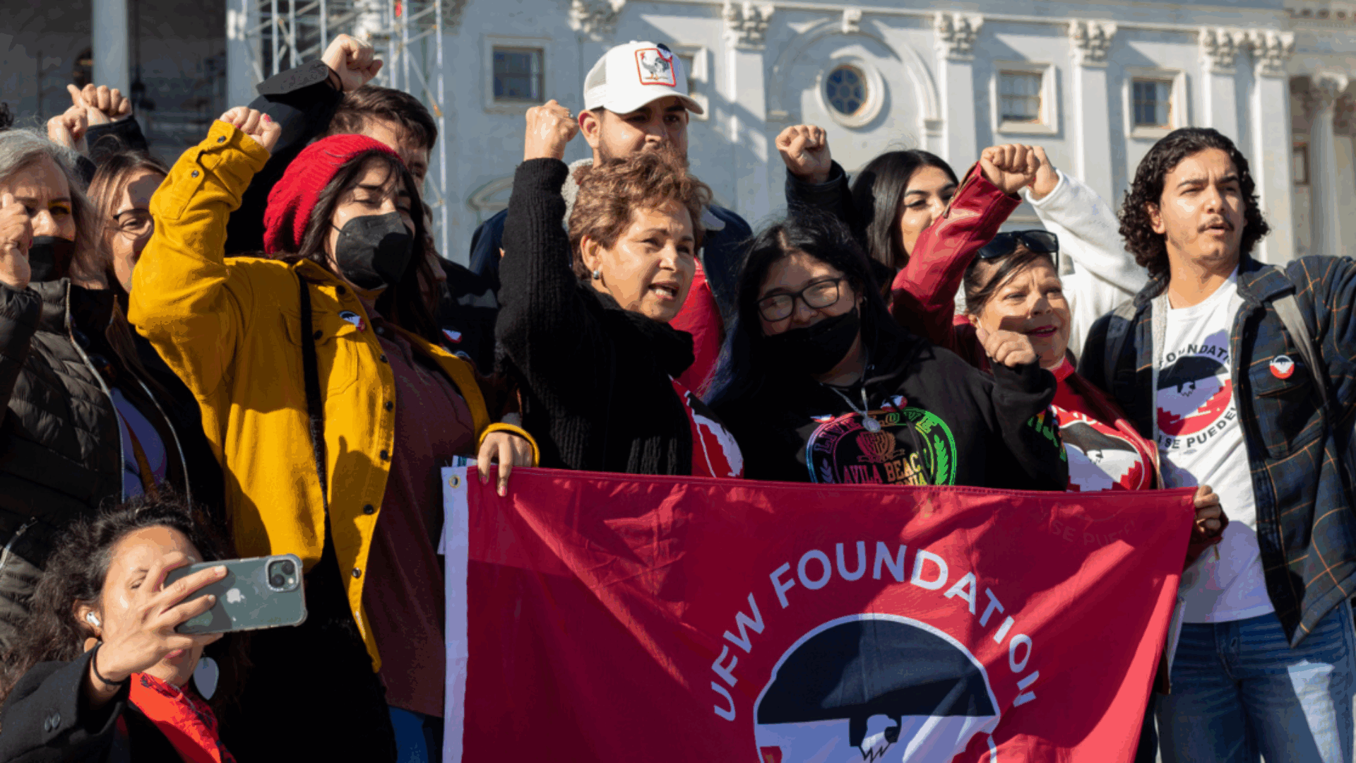 Varias personas están de pie juntas, levantando una bandera roja brillante bajo un cielo despejado.